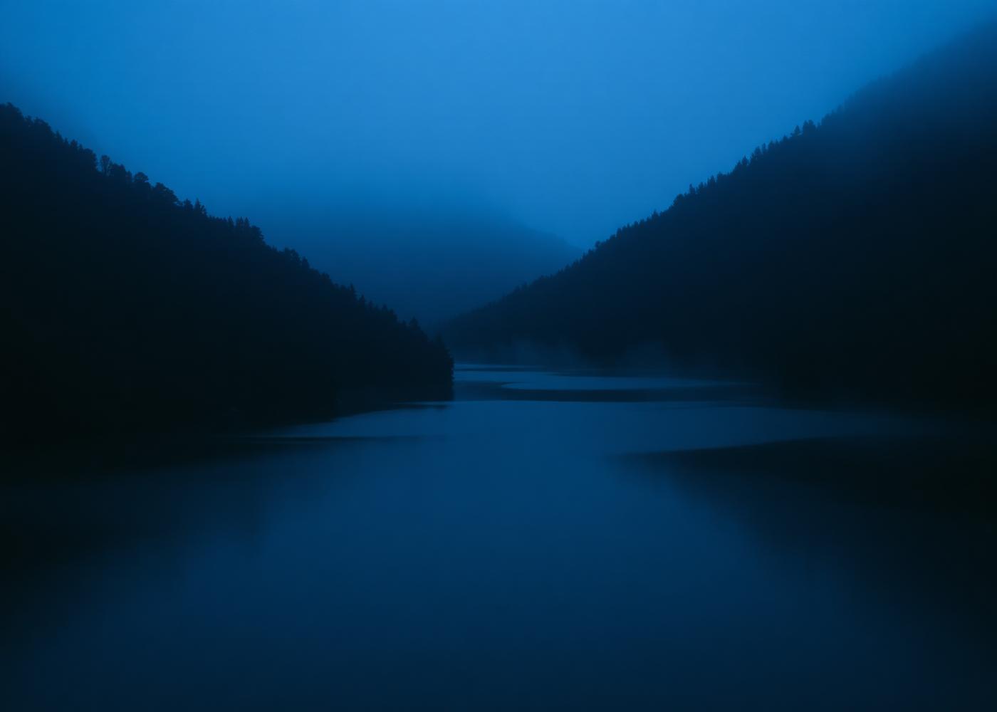 Still reservoir between forested hills at blue hour